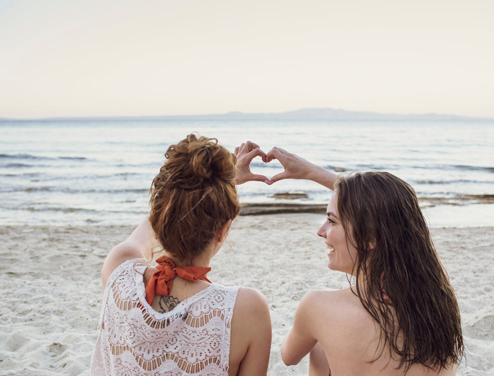 Two girls on a beach making a heart shape with their hands