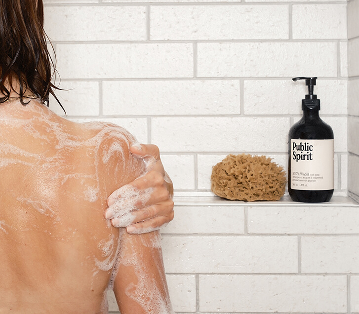 A woman in shower lathering with Public Spirit Body Wash
