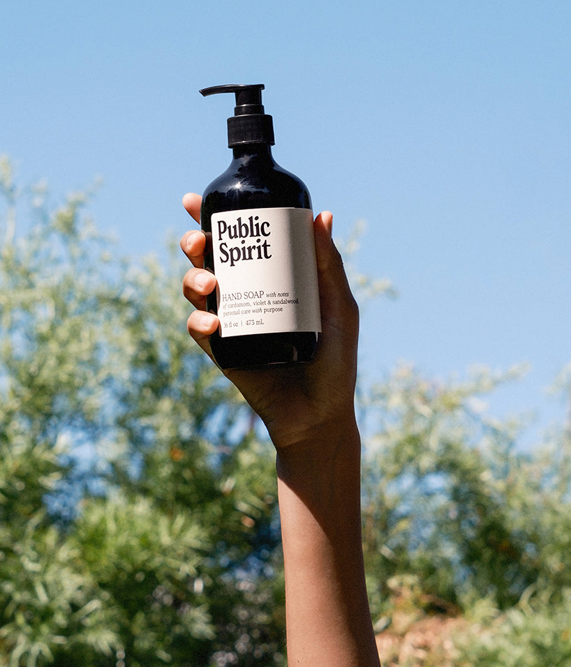 Public Spirit hand soap being held up in air with sky and trees in background